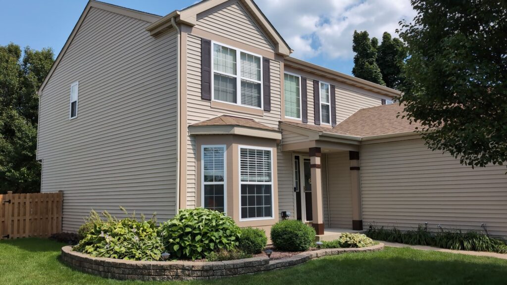 Two-story home painted in a soft beige exterior color with a bay window