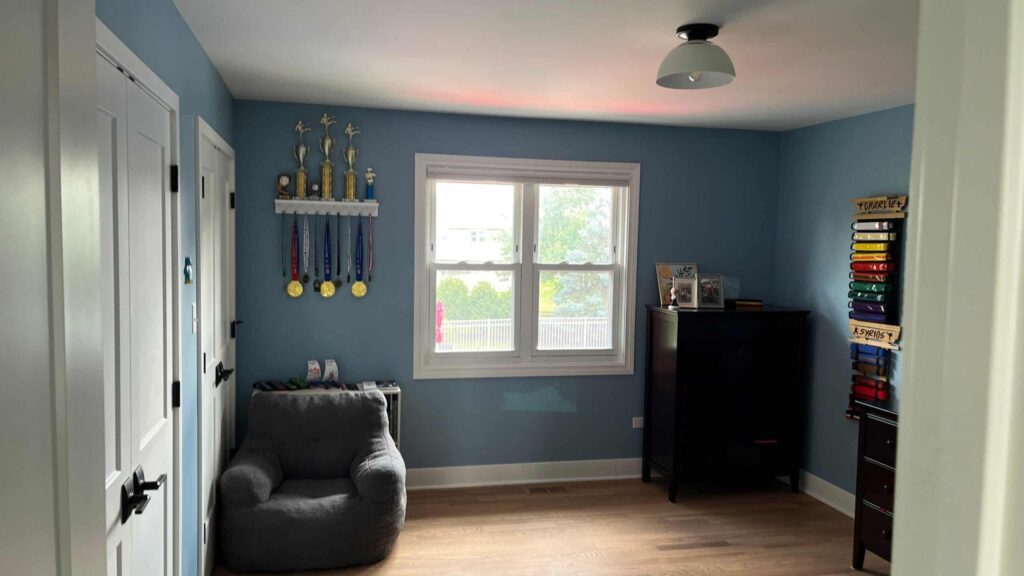 Bedroom with soft blue painted walls, a gray armchair and light wood flooring