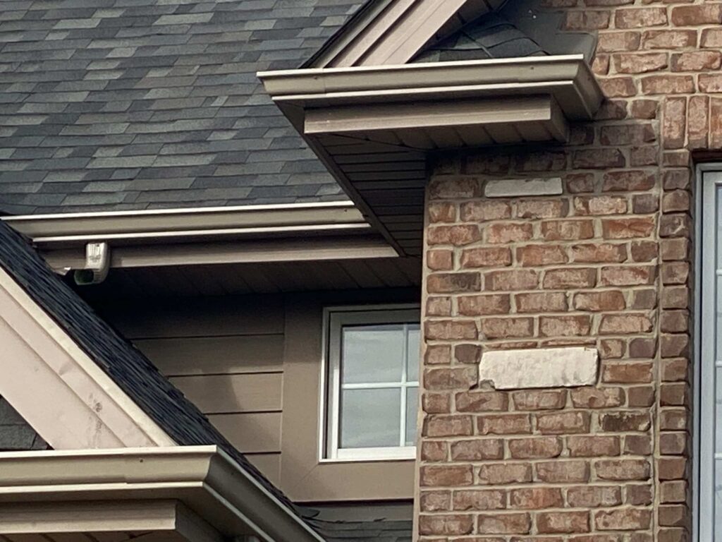 Roofline detail with a brick chimney and dark painted siding protected from weather