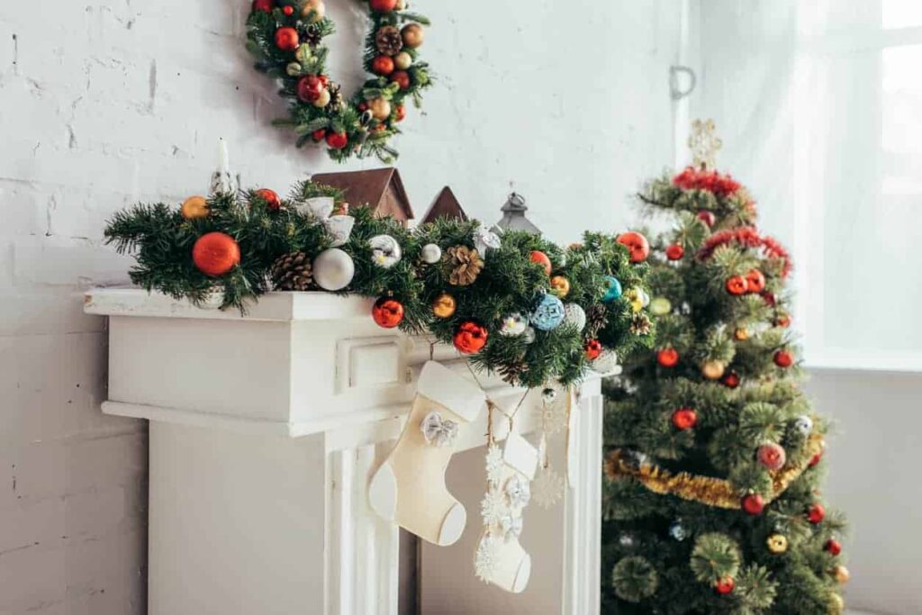 White painted fireplace mantel decorated with garland, stockings and a Christmas tree