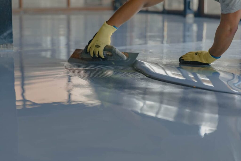 Gloved hands spreading epoxy floor coating with a squeegee in Minooka, Illinois