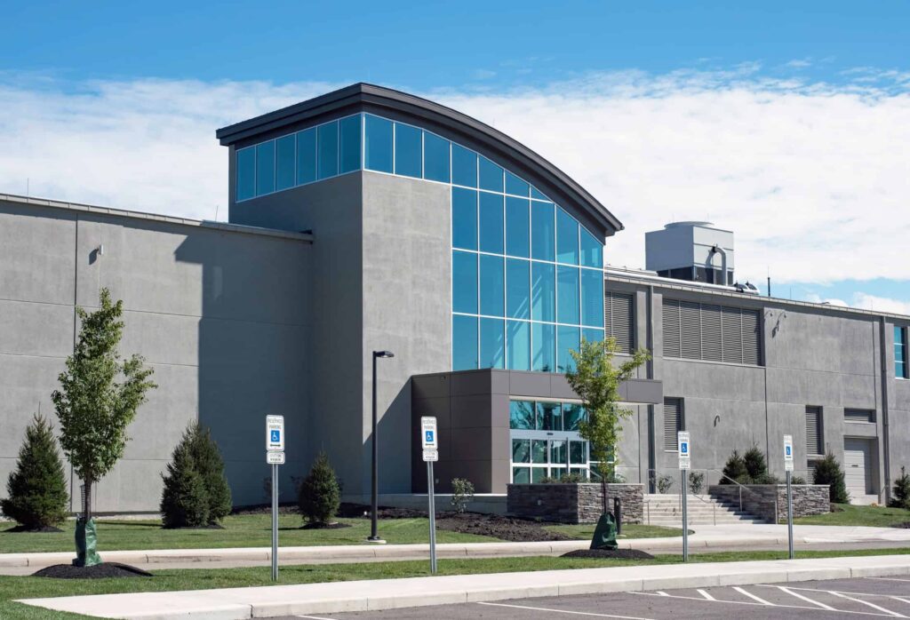 Modern commercial building with gray concrete walls and a curved blue glass entrance