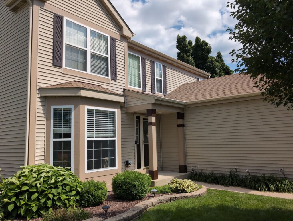 Tan two-story home with dark shutters painted during mild exterior conditions