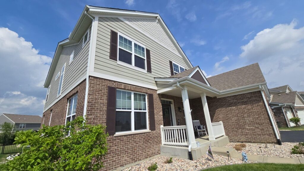 Two-story home with light siding and a brick base showing exterior paint in full sun