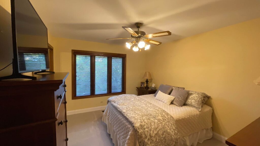 Bedroom with warm gold painted walls, a made bed and shuttered window
