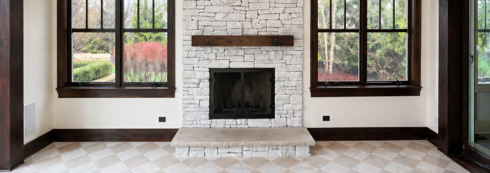 Limewashed stone fireplace with a wood mantel framed by black windows