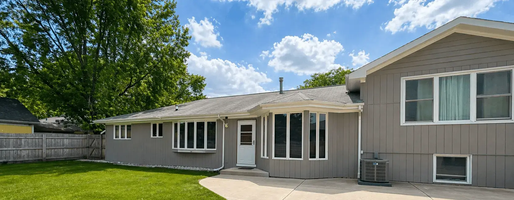 Gray ranch home rear exterior with fresh siding paint and a green lawn in Plainfield, Illinois