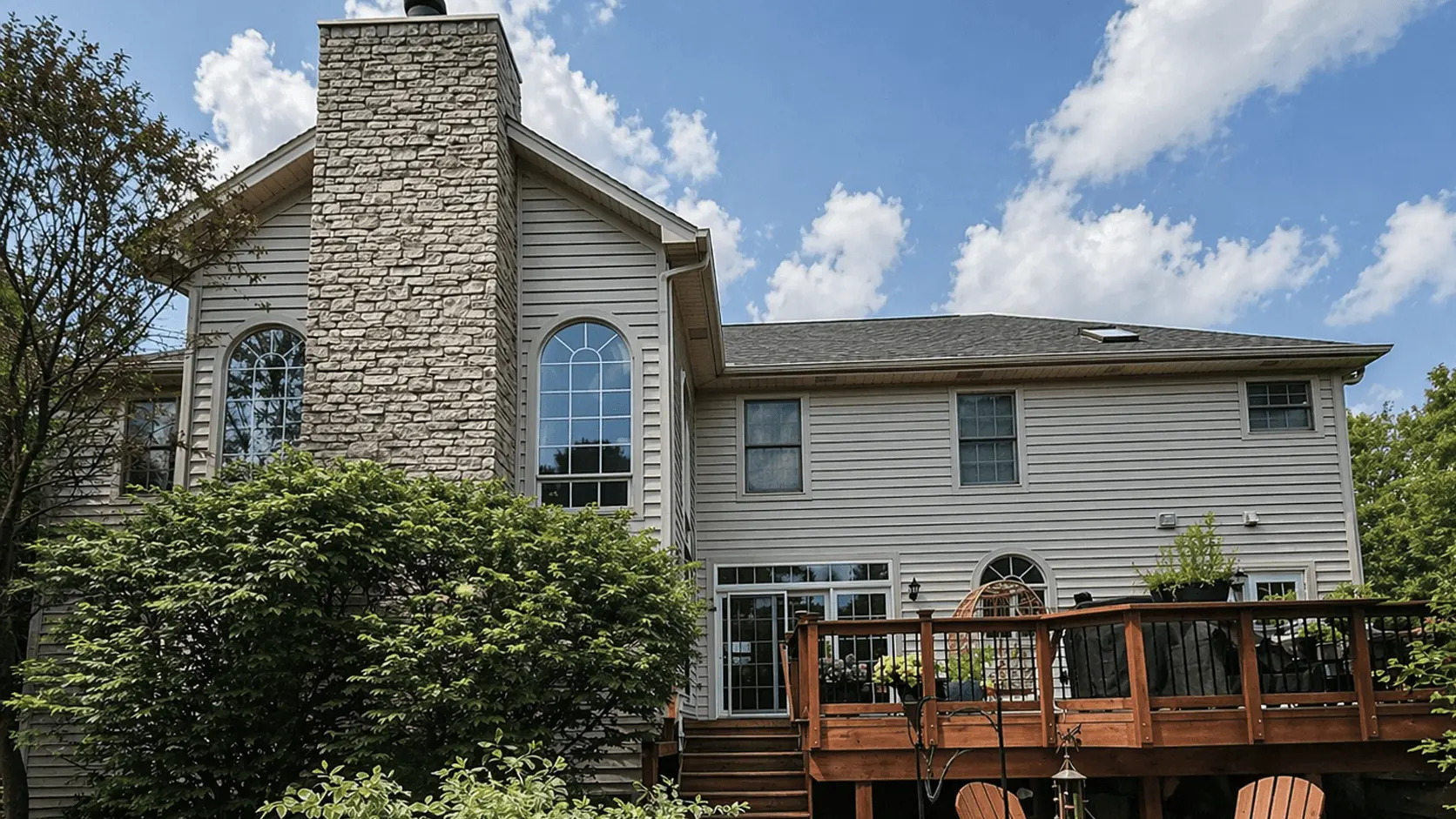 Two-story home with stone chimney, gray siding and a stained wood deck after exterior painting