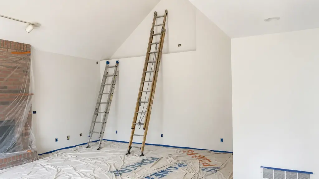 Two-story family room in a Plainfield home with ladders set up and floors covered before repainting